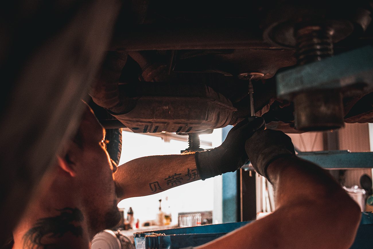 Mechaniker arbeitet unter einem aufgebockten Fahrzeug am Auspuff