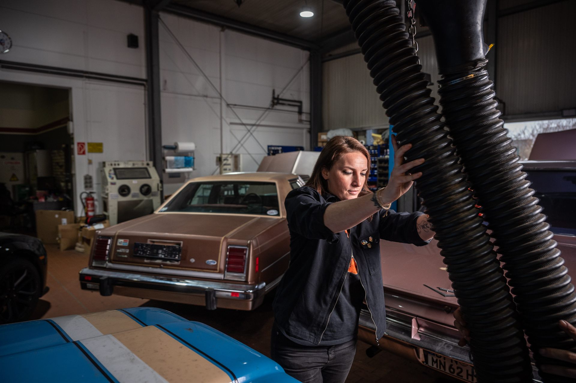 Maja Hofmann in der Werkstatthalle von Deine Autostube, im Hintergrund ein brauner amerikanischer Klassiker